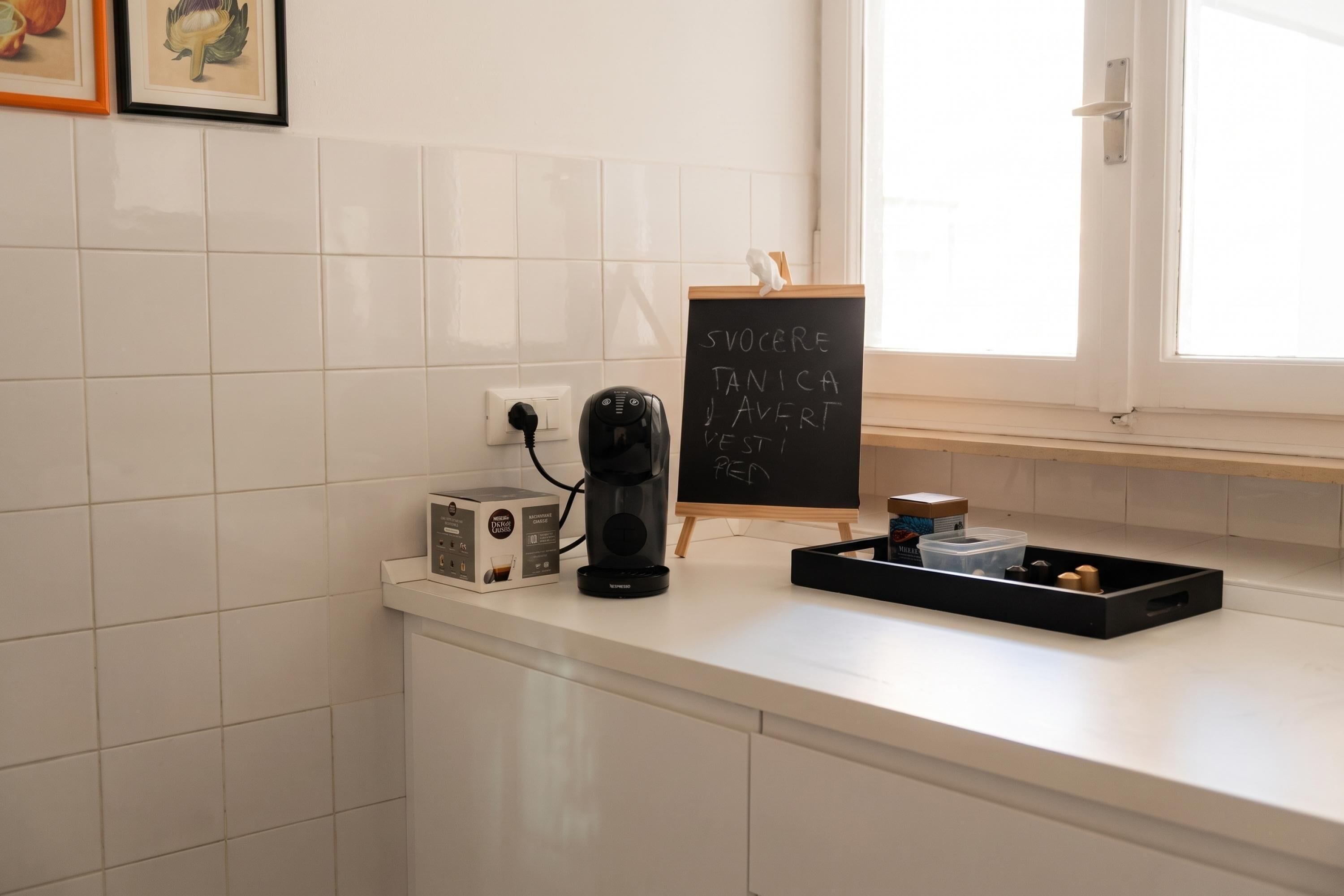 Un piano di lavoro in cucina con una macchina da caffè, un tostapane e una lavagna con scritte.
