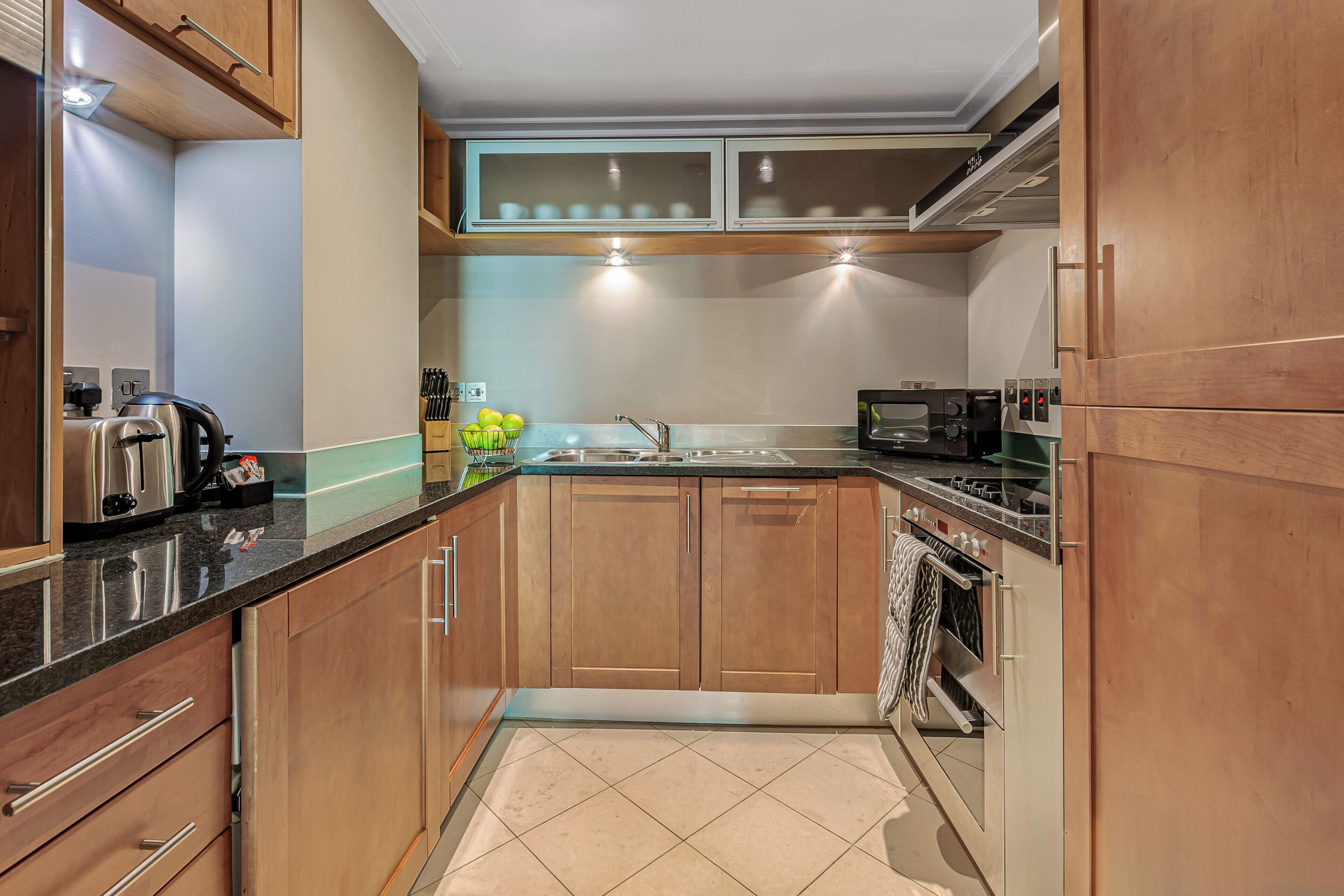 A compact kitchen with wooden cabinets, a stainless steel range hood, and a built-in microwave.