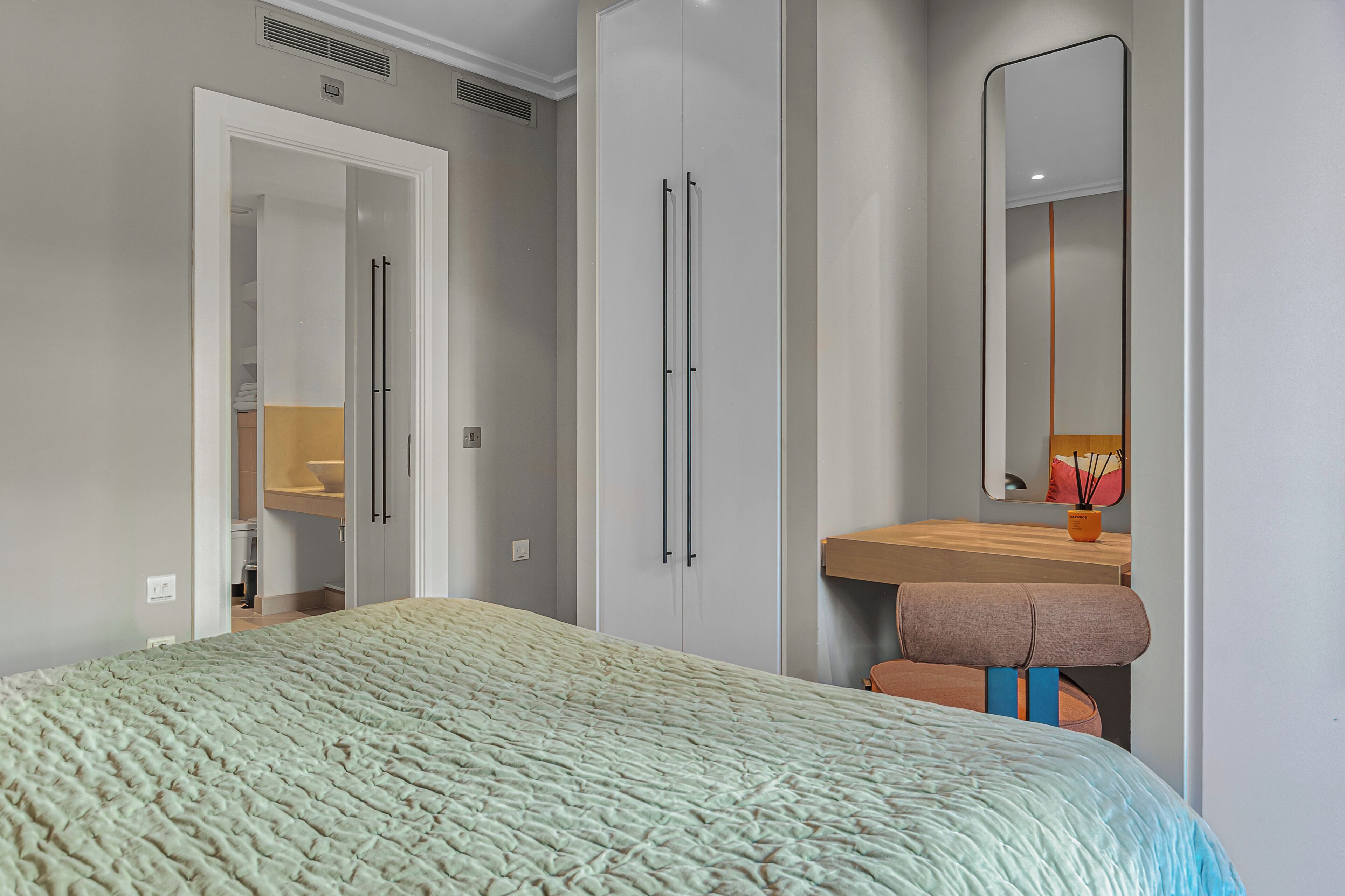 Una camera da letto con un letto, un armadio, uno specchio e un bagno visibile attraverso una porta aperta.