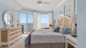 Un dormitorio con una cama grande, un aparador, un ventilador de techo y vista al océano.