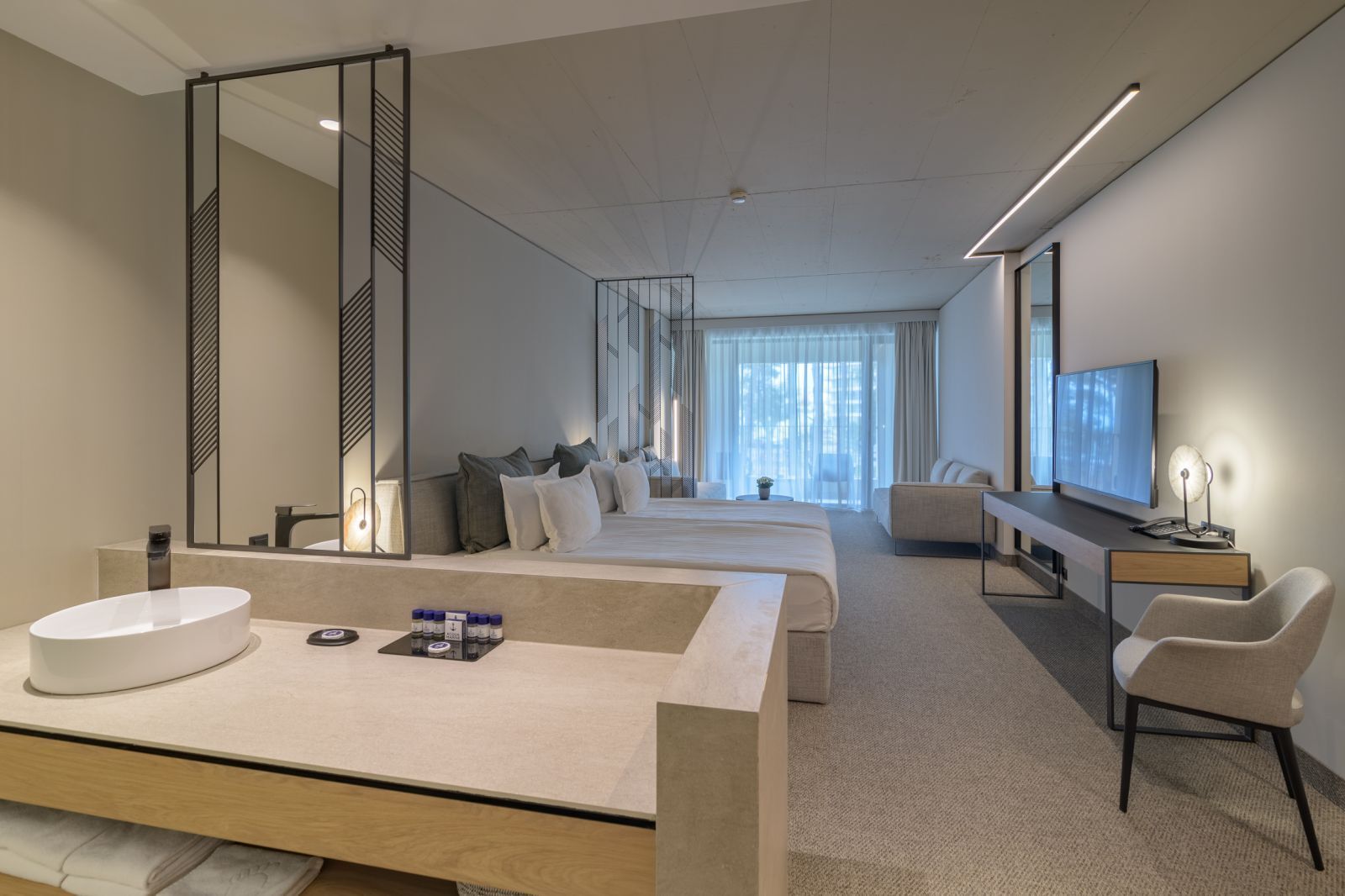 Une chambre d’hôtel moderne dotée d’un grand lit, d’un canapé séparé, d’un bureau avec une télévision et d’un grand miroir.