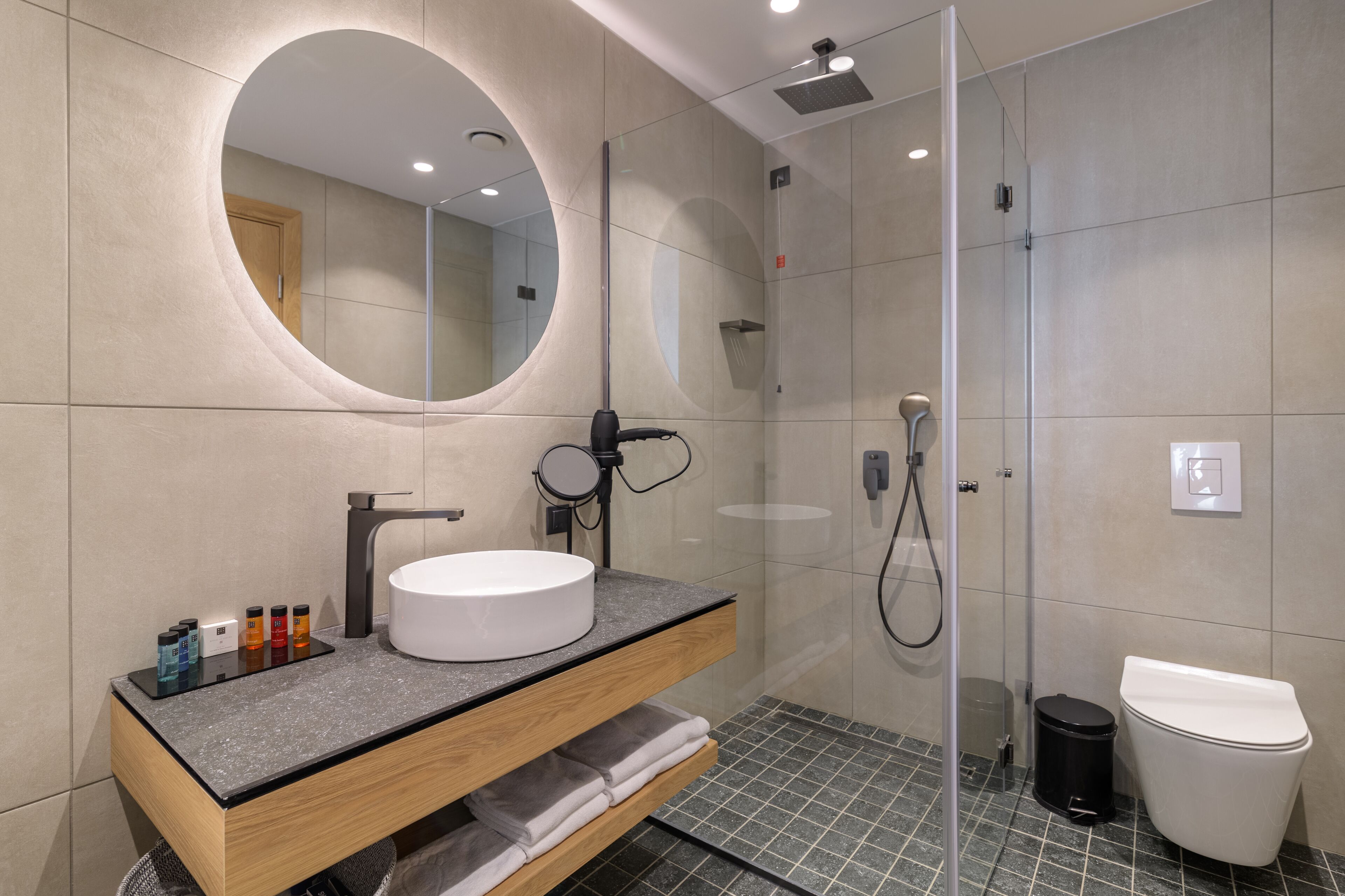 Un baño moderno con un espejo redondo, un lavabo blanco y una zona de ducha.
