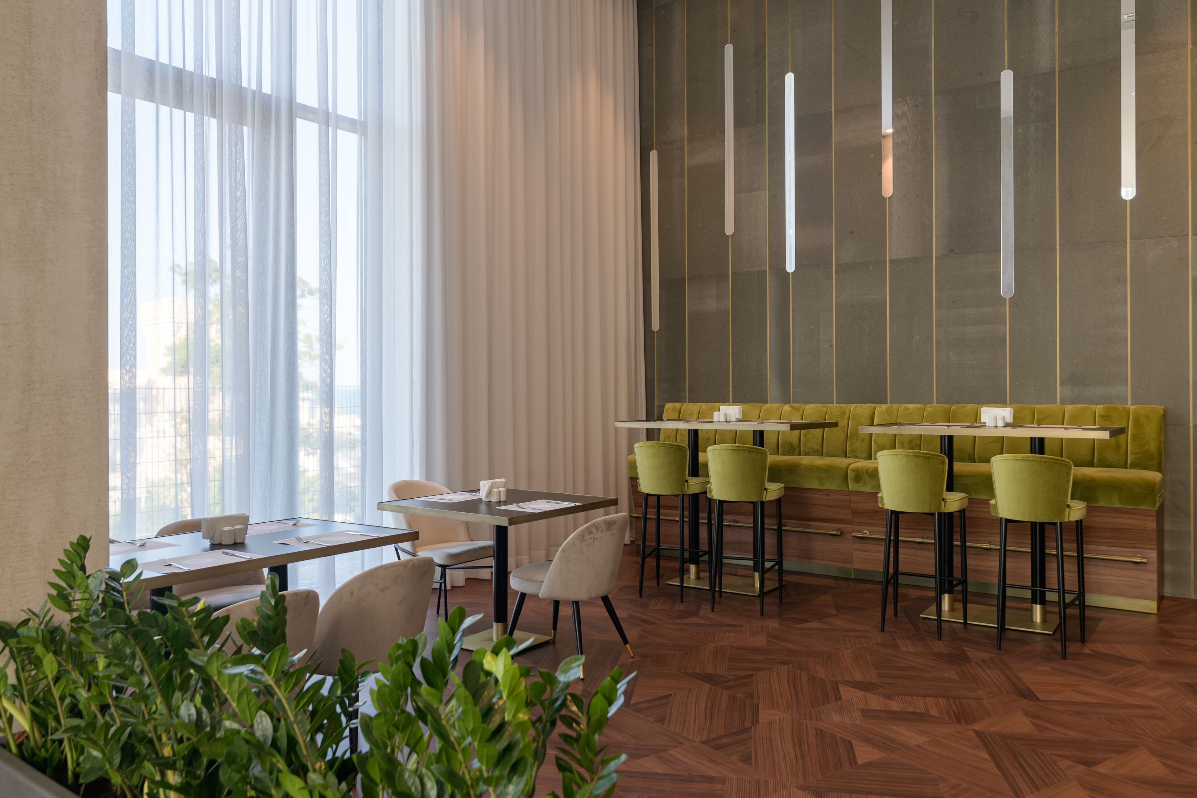 Uma sala de jantar moderna com piso em padrão herringbone de madeira, banquetas de bar verdes e um banco estofado verde.