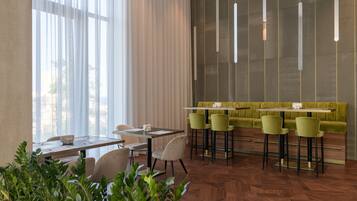 Uma sala de jantar moderna com piso em padrão herringbone de madeira, banquetas de bar verdes e um banco estofado verde.