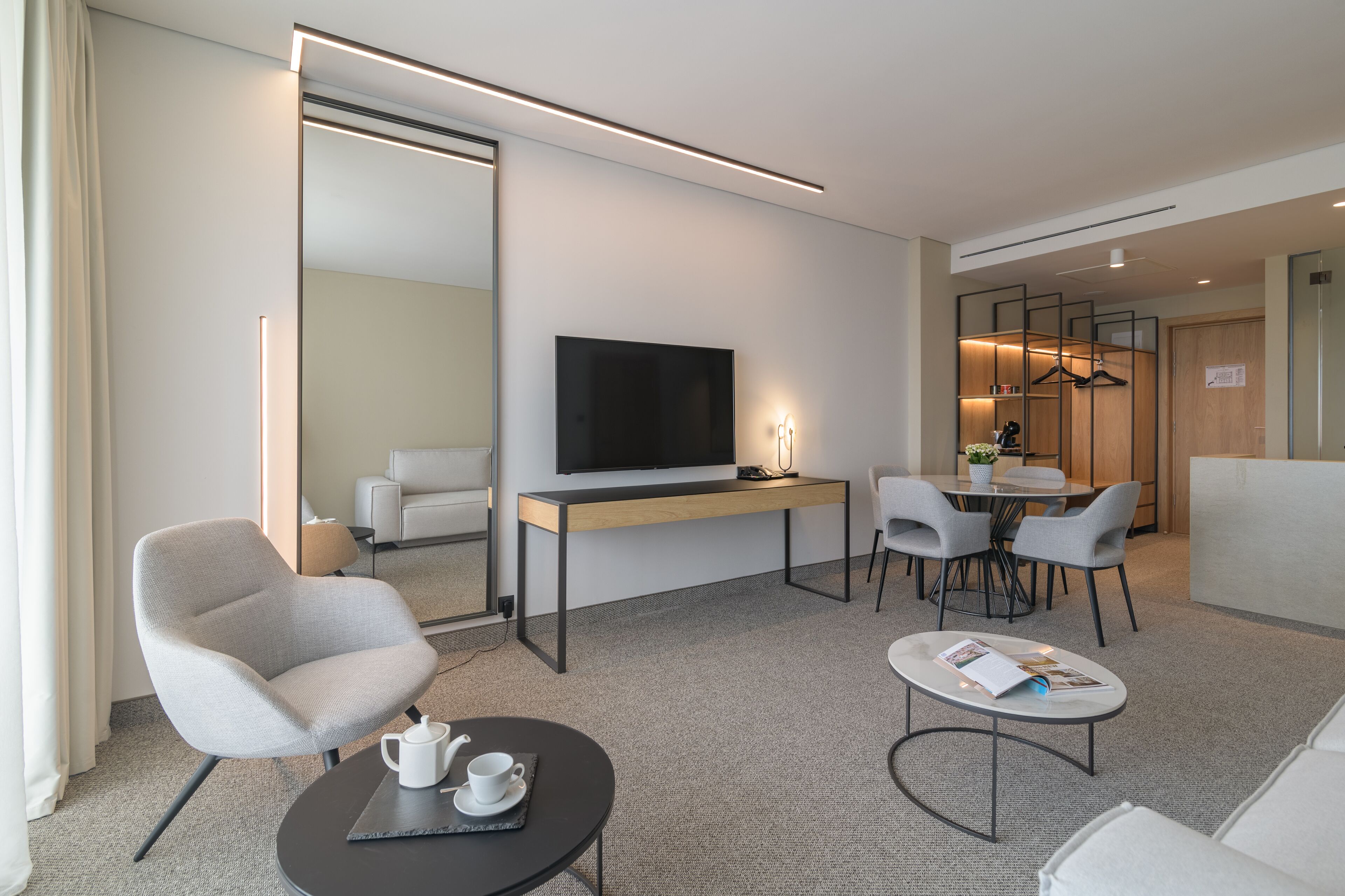 A modern hotel room with a flat-screen TV, a desk, a dining area, and a seating arrangement.