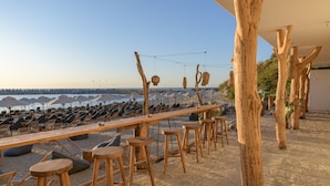 Un bar situé en bord de mer, avec des tabourets et des tables en bois, offrant une vue sur l’océan.
