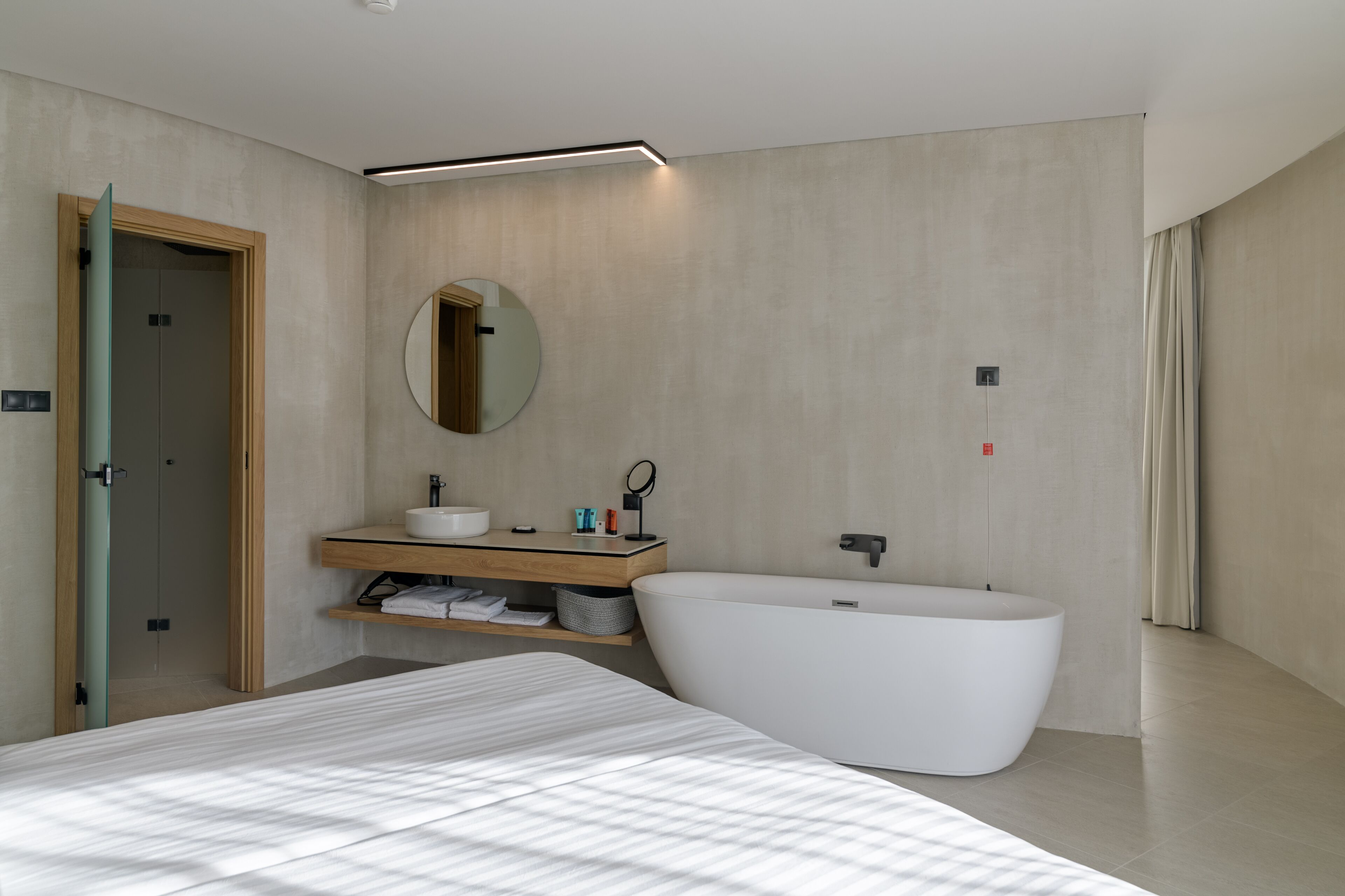 Un baño moderno con una bañera independiente, un espejo redondo y un tocador de madera.