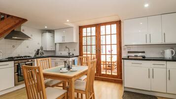 Une cuisine moderne avec des meubles blancs, une table à manger avec des chaises, une cuisinière et une fenêtre donnant sur l’extérieur.
