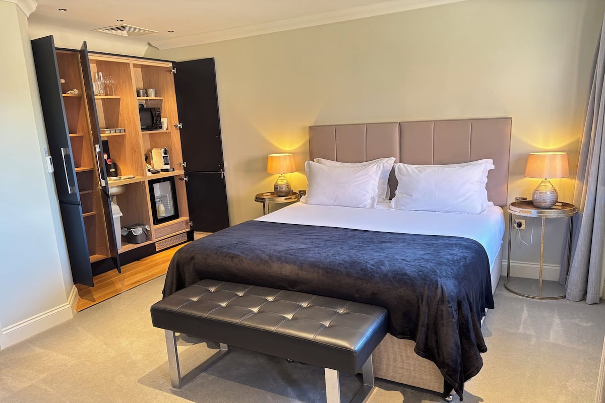 A hotel room with a bed, bedside lamps, a bench, a wardrobe, and a small table.