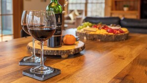 Une table en bois avec deux verres à vin et une bouteille de vin, une assiette de fruits et un sous-verre en bois.