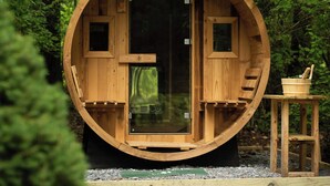 Une structure cylindrique en bois dotée d’une porte en verre, une petite table en bois avec un bol et une cuillère, et un banc en bois à l’intérieur.
