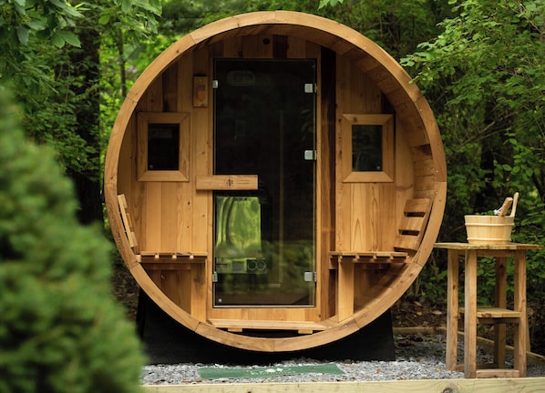 Une structure cylindrique en bois dotée d’une porte en verre, une petite table en bois avec un bol et une cuillère, et un banc en bois à l’intérieur.