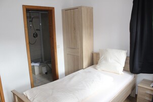 Un dormitorio con cama, armario, mesita de noche y zona de ducha.