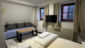 Una habitación con cama, sofá, mesa, televisor y ventana con cortinas.