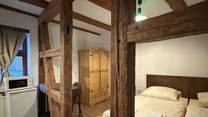 Una habitación rústica con vigas de madera a la vista, una cama, un armario de madera, una mesita y una kitchenette con microondas.