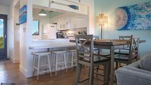Een moderne keuken met een centraal eiland, barkrukken en een eettafel met stoelen.