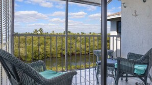 Een balkon met rieten meubilair, uitzicht op een waterpartij en een heldere lucht.