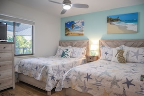 A bedroom with two beds, a ceiling fan, a nightstand with a lamp, and artwork on the walls.