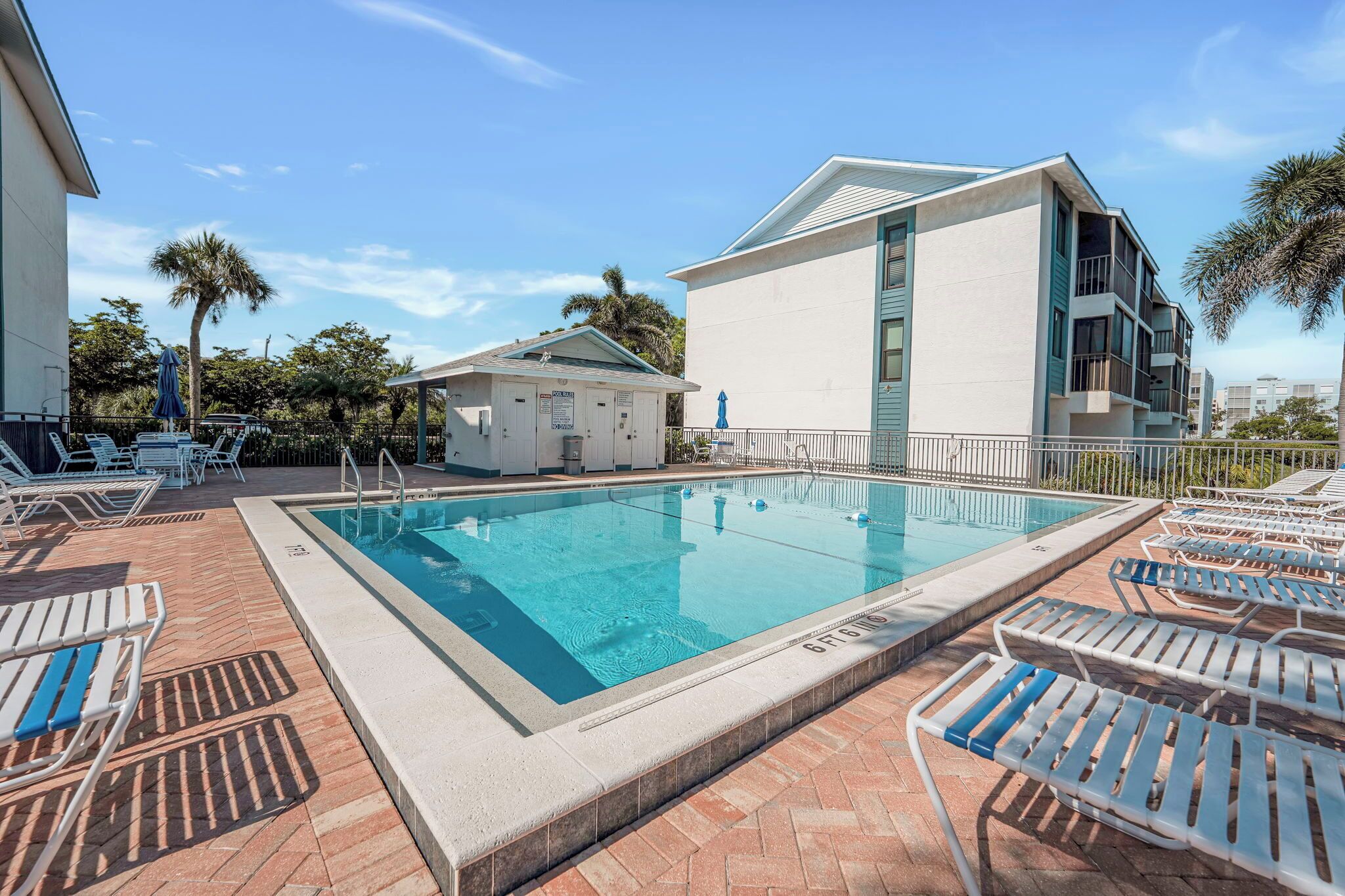 Une piscine avec des chaises longues, un petit bâtiment et un immeuble à plusieurs étages doté de balcons.