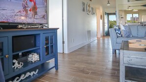 Een woonkamer met een televisie op een blauwe kast, een grijze bank en een houten salontafel.