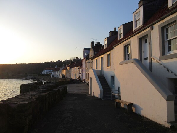 A coastal street with terraced houses, a stone wall, and a bench.