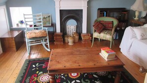 A cozy living room with a fireplace, a wooden coffee table, a rocking chair, and a bookshelf.