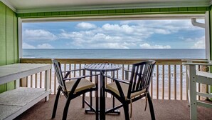 A covered outdoor seating area with a table and chairs, overlooking a beach with the ocean and a cloudy sky. - 2 Bedroom Oceanfront Condo with Beautiful Views (Surf City)
