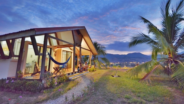 A modern house with a glass facade, a hammock, and a view of mountains.