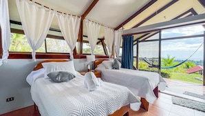 A hotel room with two beds, a large window with a view of the outdoors, and a hammock outside.