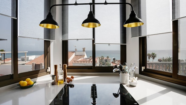Une cuisine moderne dotée d’une grande fenêtre offrant une vue sur la côte, d’une plaque de cuisson à induction noire et d’un design minimaliste.
