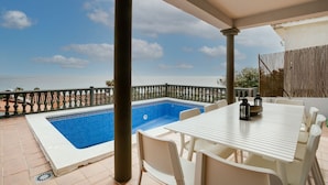 Une terrasse avec une piscine, une table et des chaises blanches, et une vue sur la mer.