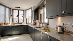 Une cuisine moderne avec des meubles de couleur sombre, un plan de travail en marbre et des luminaires suspendus.