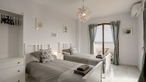 Une chambre avec deux lits, une armoire, un luminaire au plafond et une vue sur la mer.
