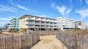 A beachfront hotel with multiple balconies, a sandy walkway, and a wooden fence. - Beachcrest 17-Oceanfront 76th St, Free WiFi, AC (Ocean City)
