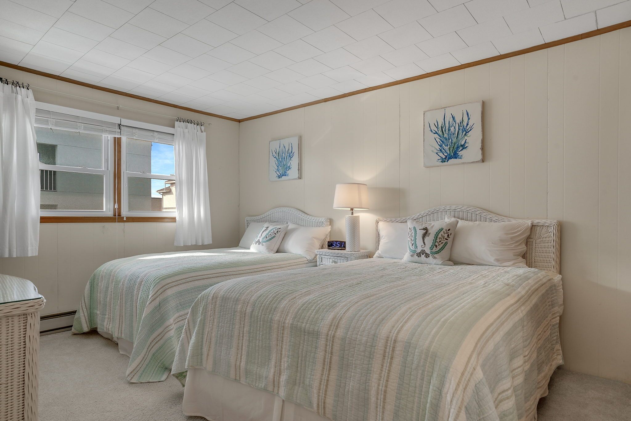 A bedroom with two beds, a bedside table with a lamp, and a wall clock.