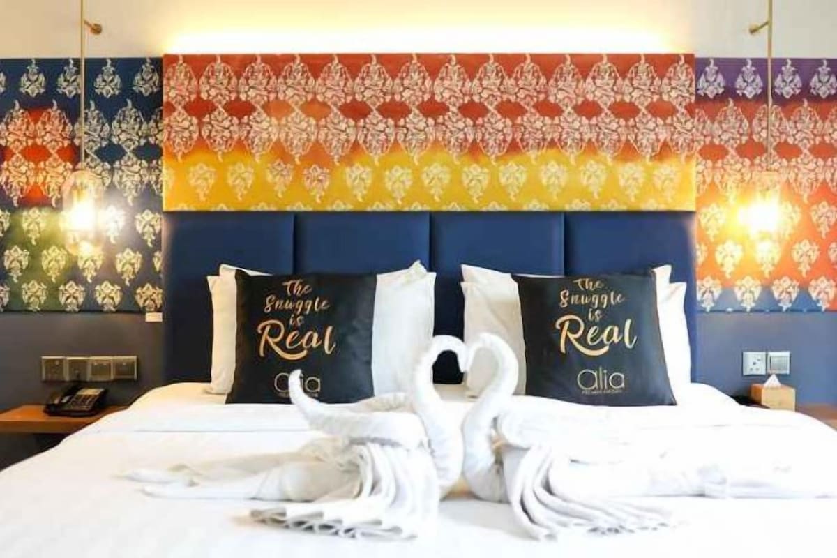 A hotel room with a bed, two pillows with text, a wall with a pattern, and a nightstand with a phone.