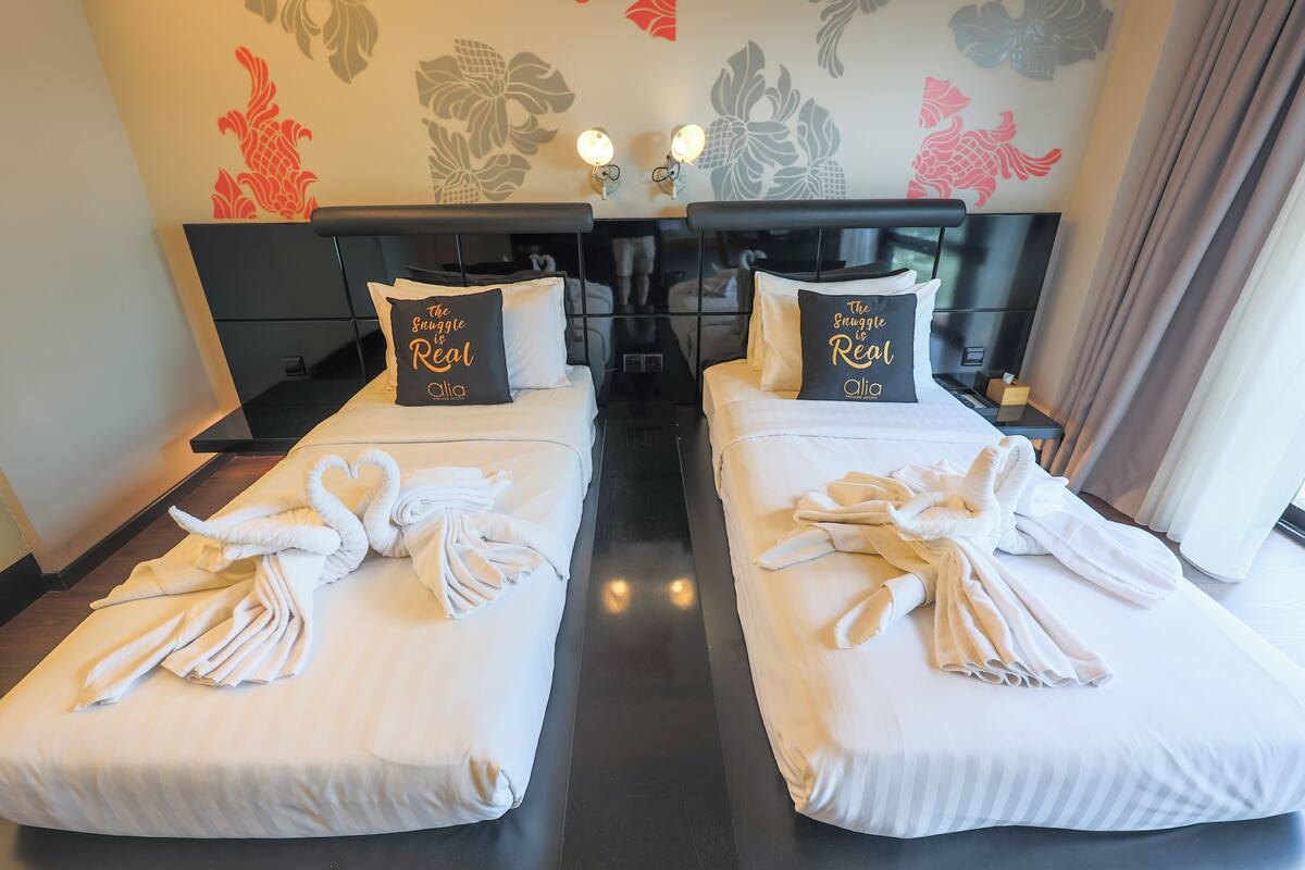 Two twin beds with white linens and matching pillows, a headboard with a mirror, and wall art with floral patterns.