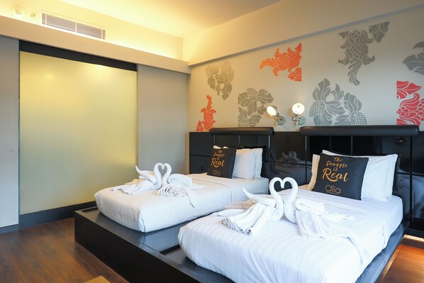 Ein Hotelzimmer mit zwei Betten, jeweils mit weißen Leintüchern und Handtüchern, die zu Schwänen geformt sind. Das Zimmer besticht durch ein modernes Design mit einem dunklen Kopfteil und einer Wand, die mit floralen Mustern verziert ist.