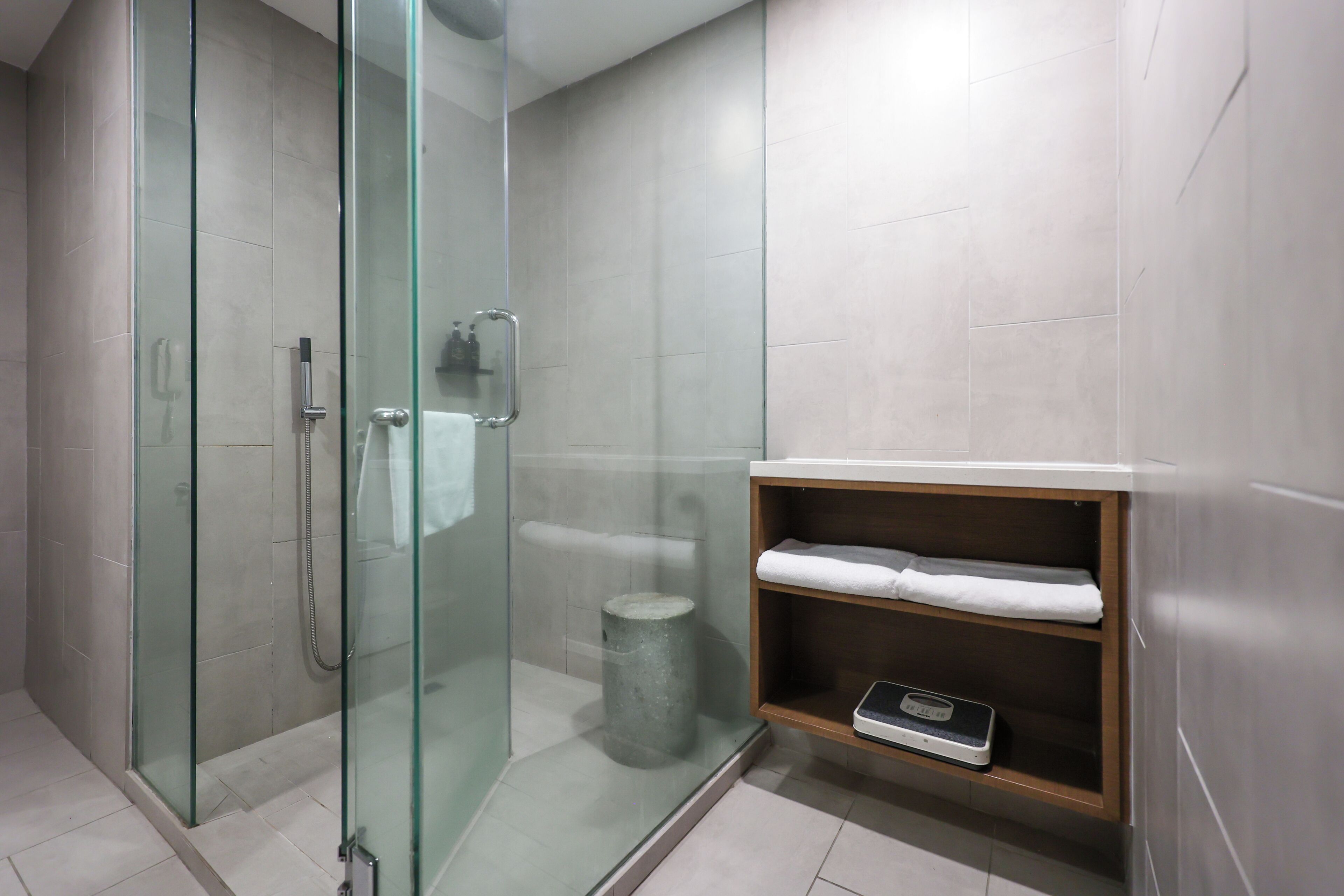 A modern bathroom with a glass-enclosed shower, a wooden shelf with towels, and a scale.