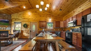 Ein Holzblockhaus mit Esstisch, Küchenzeile und Kamin.