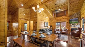Ein Holzblockbau-Innenraum mit Essbereich, Sofas, einem Kamin und einem Fernseher.