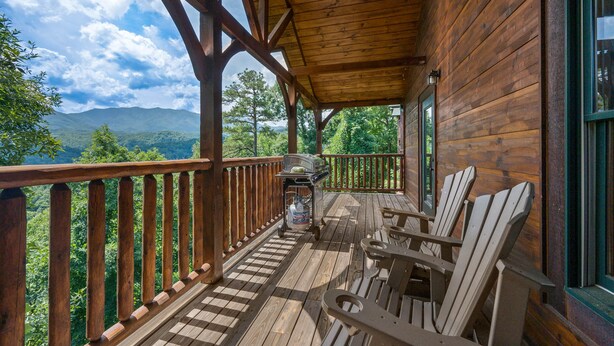 Eine Holzterrasse mit Adirondack-Stühlen und einem Grill, mit Blick auf eine gebirgige Landschaft.