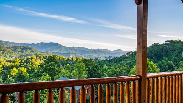 A wooden balcony railing overlooking a mountainous landscape with dense greenery and distant buildings. - Gorgeous Views, Hot Tub, Game Room, and Free Attraction Passes, Resort Pool (Gatlinburg,)