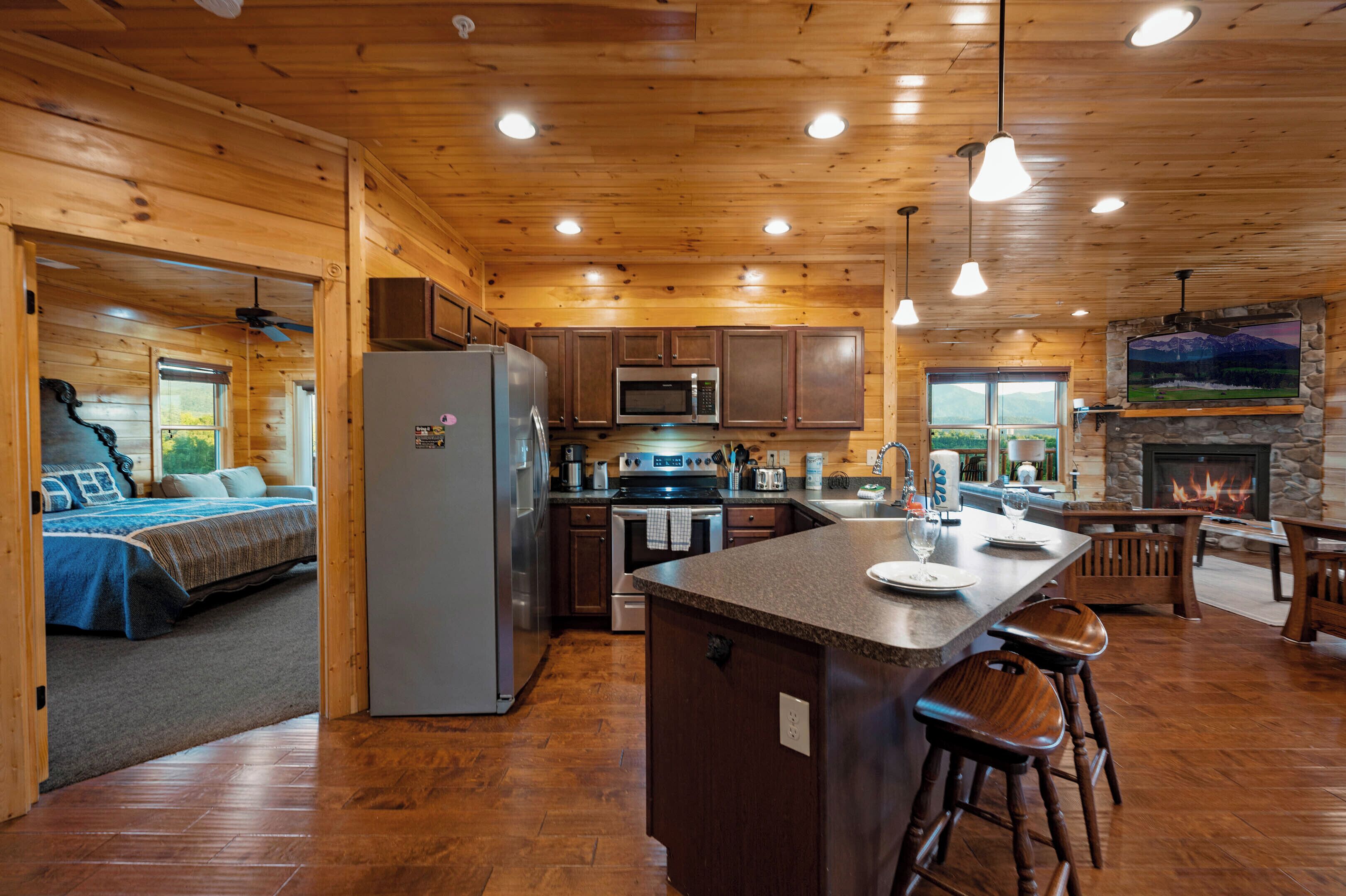 A log cabin interior with a kitchen, dining area, and a bedroom with a view.