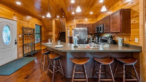 A wooden cabin interior with a kitchen, bar area, and a staircase. - Gorgeous Views, Hot Tub, Game Room, and Free Attraction Passes, Resort Pool (Gatlinburg,)