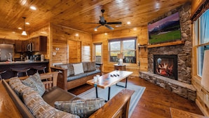 A log cabin interior with a stone fireplace, wooden furniture, and a television mounted above it. - Gorgeous Views, Hot Tub, Game Room, and Free Attraction Passes, Resort Pool (Gatlinburg,)