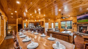 A spacious wooden cabin with a large dining table set for six, a kitchen area, and a fireplace. - Gorgeous Views, Hot Tub, Game Room, and Free Attraction Passes, Resort Pool (Gatlinburg,)