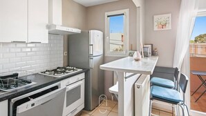 A compact kitchen with white cabinets, a gas stove, a built-in oven, and a refrigerator. There is a small dining area with a table and chairs. - Hyères T2 5mn plage Almanarre CLiM/PK/WiFi (HYERES)
