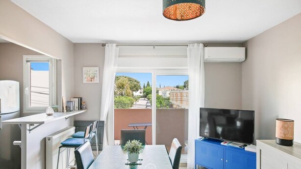 A modern apartment with a dining area, a TV, and a balcony with a view of the city. - Hyères T2 5mn plage Almanarre CLiM/PK/WiFi (HYERES)