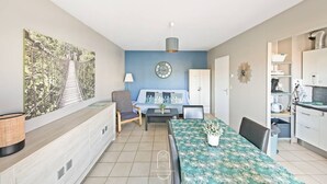 A modern living room with a sofa, a dining table, and a kitchen area. - Hyères T2 5mn plage Almanarre CLiM/PK/WiFi (HYERES)